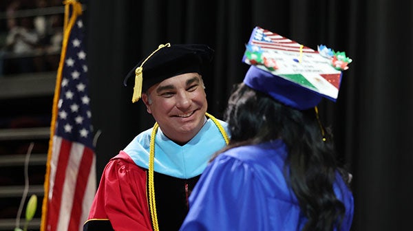 Faculty member congratulating a graduate on stage during commencement ceremony.